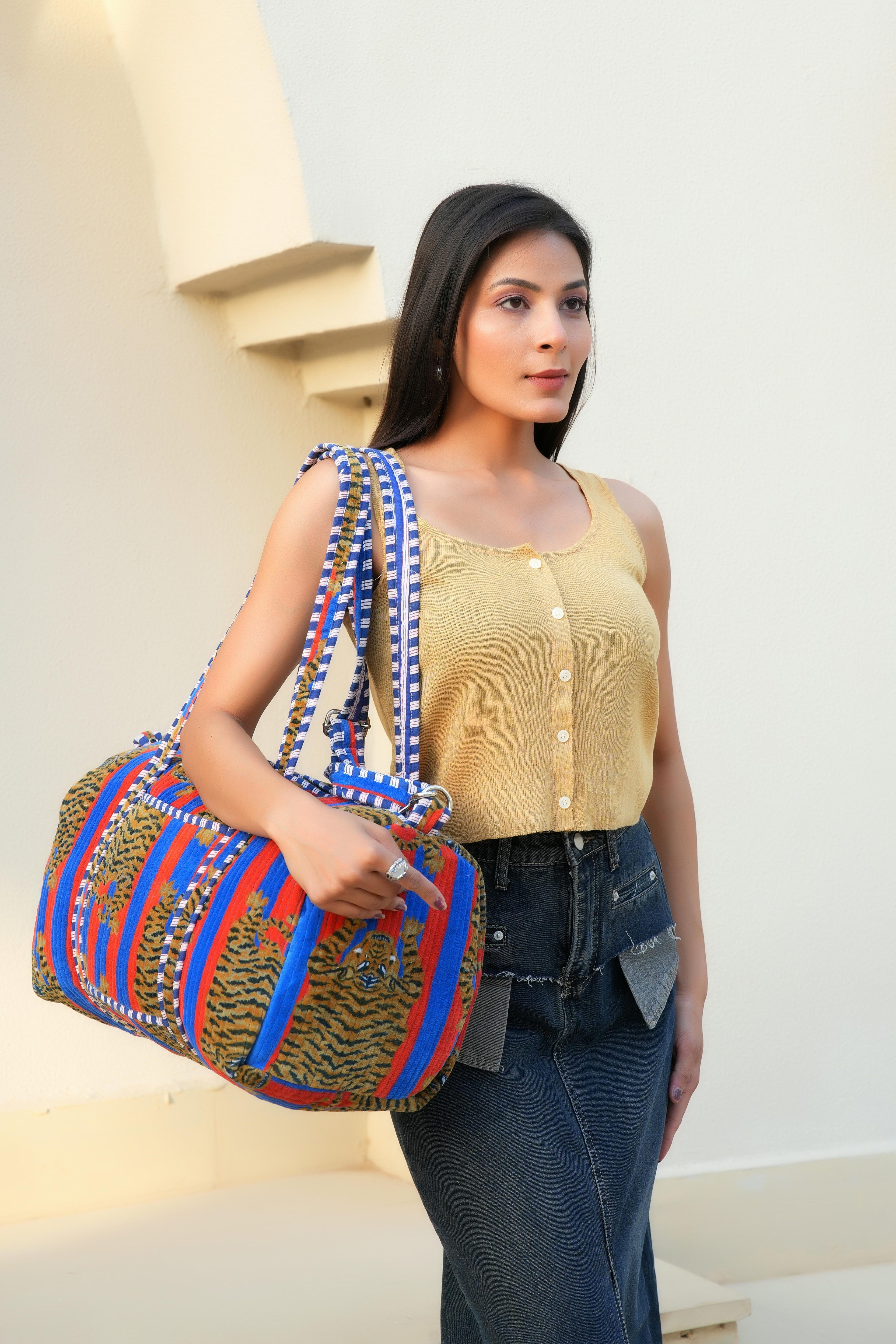Model carrying The Tibetan Tiger Velvet Weekender by the top handles, walking through a sunlit terminal