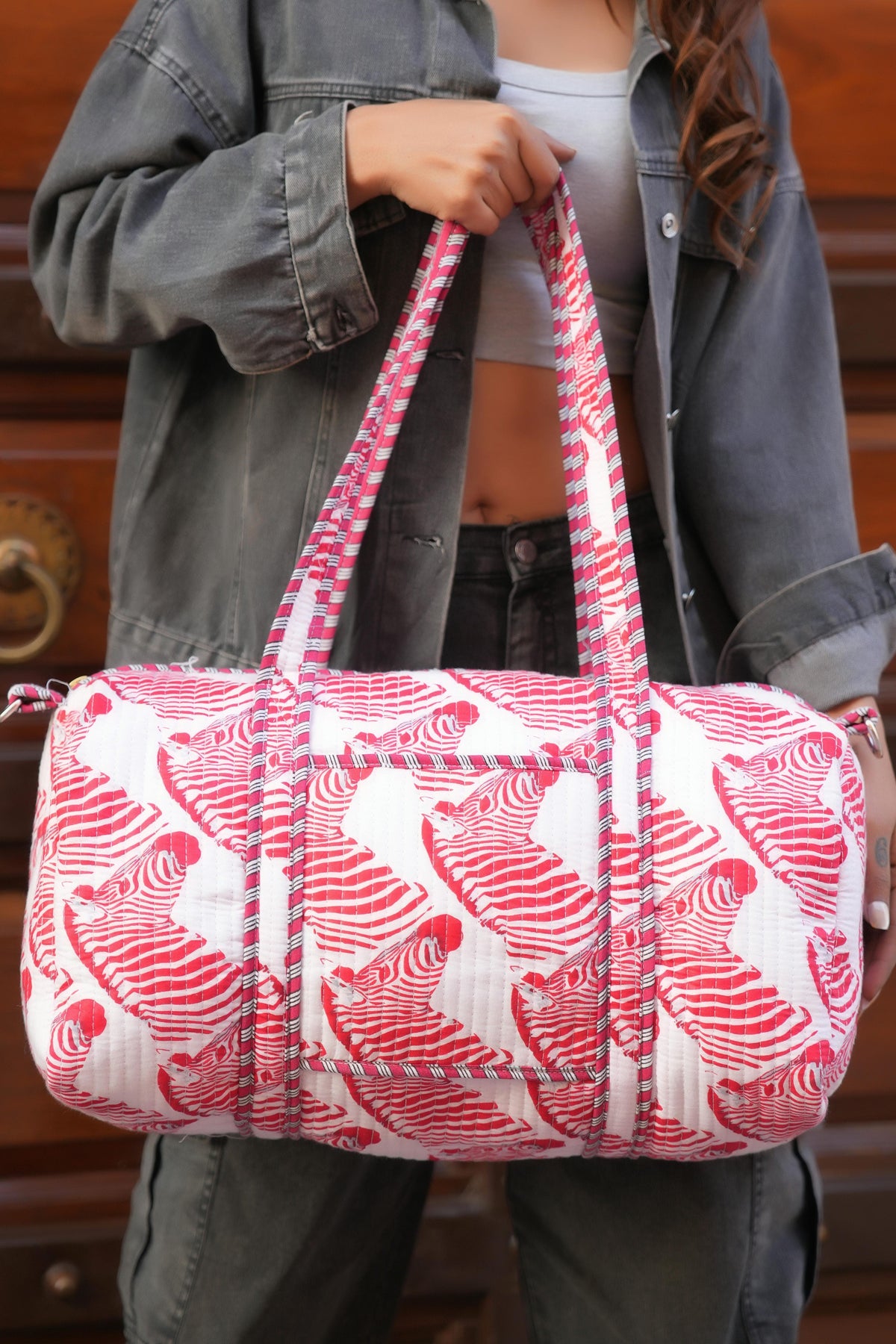 The Zebra Weekender in pink, close-up with the handles gathered in one fist: handmade cotton weekender, ethically crafted in Rajasthan.