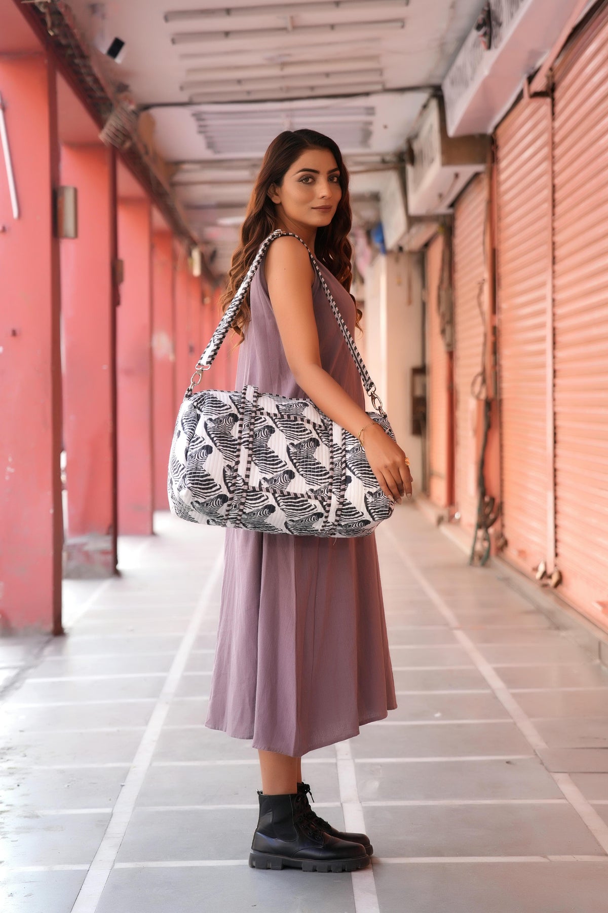 The Zebra Weekender on the shoulder as the model glances back, rear three-quarter: handmade cotton weekender, ethically crafted in Rajasthan.