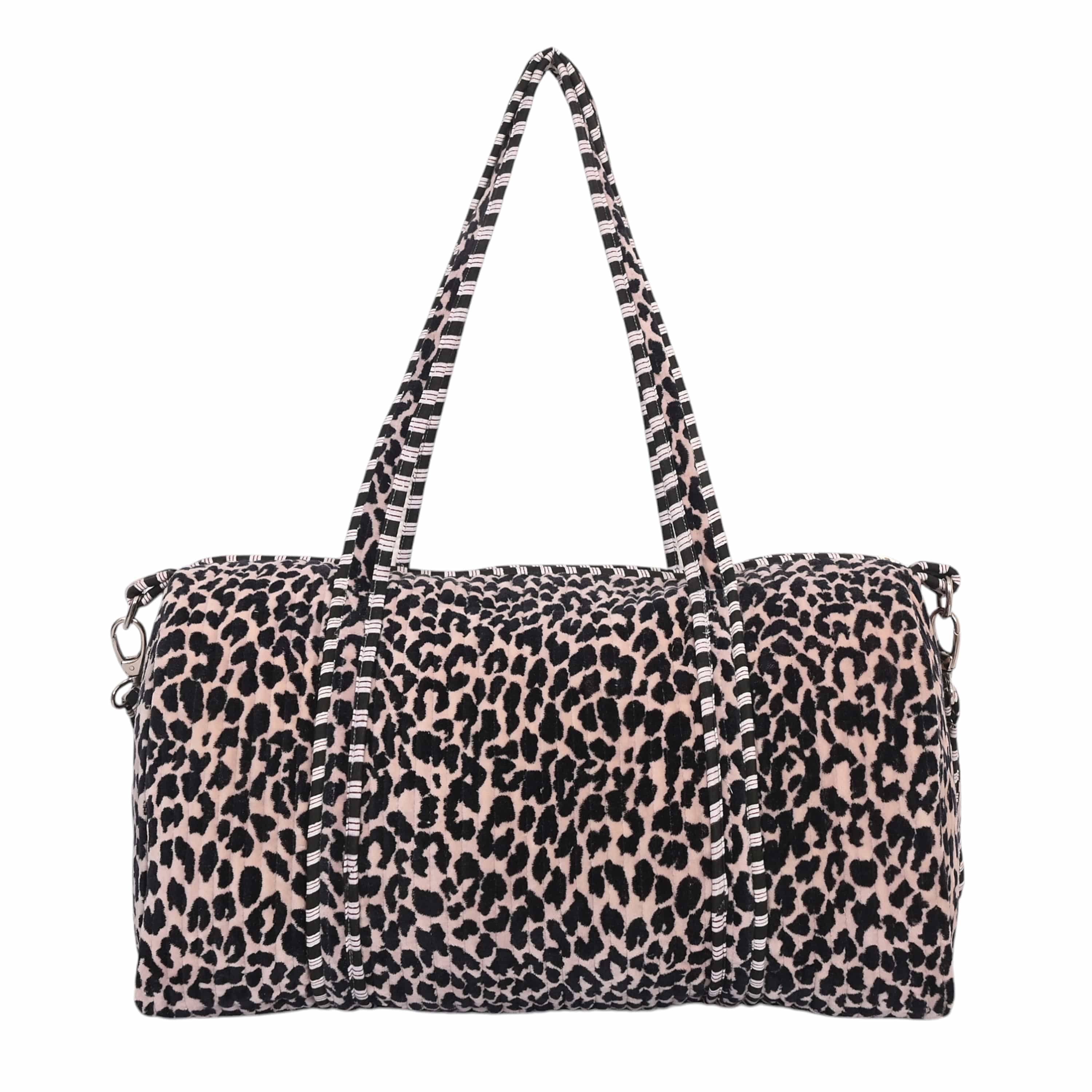 Model carrying The Velvet Leopard Weekender by the top handles, walking through a hotel lobby