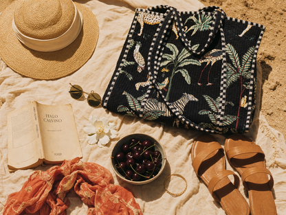 Italian holiday flatlay — straw hat, sunglasses, Italo Calvino, cherries and the Leopard Tote in black, hand-block-printed cotton from Conscious Yoga Collective