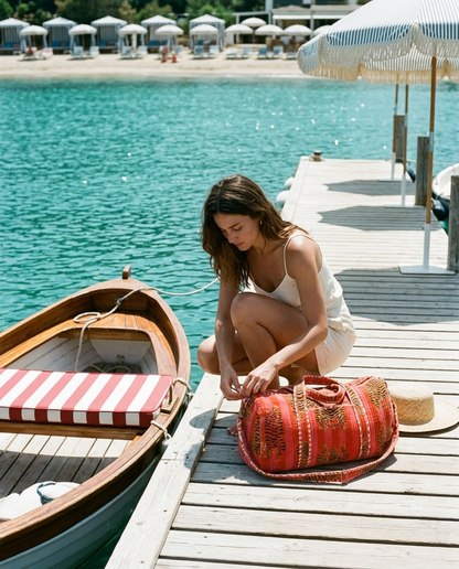 Wooden boat dock adjusting the strap of the Tibetan Tiger Velvet Weekender in Orange and Pink — handmade in Rajasthan by Conscious Yoga Collective