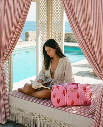 Striped cabana daybed reading with the Lobster Weekender in Pink beside her — handmade in Rajasthan by Conscious Yoga Collective