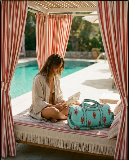 Striped cabana daybed reading with the Lobster Weekender in Turquoise beside her — handmade in Rajasthan by Conscious Yoga Collective