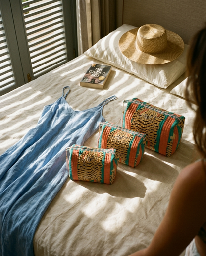 Tibetan Tiger 3 Piece Travel Set in coral and teal cotton, handmade travel pouch set ethically made in Rajasthan, on sunlit linen beside a blue dress.