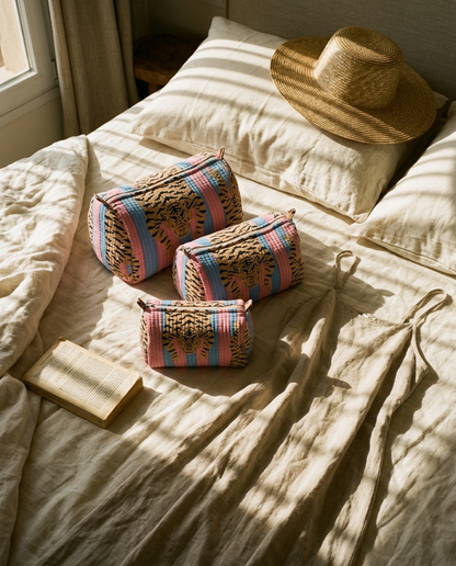 Tibetan Tiger 3 Piece Travel Set in pink and blue cotton, a handmade, ethically crafted travel pouch set from Rajasthan, on bed linen by a sunny window.