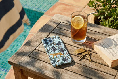 The Jungle iPhone Case in Duck Egg on a teak side table beside a chilled iced tea and a paperback at a Mediterranean pool