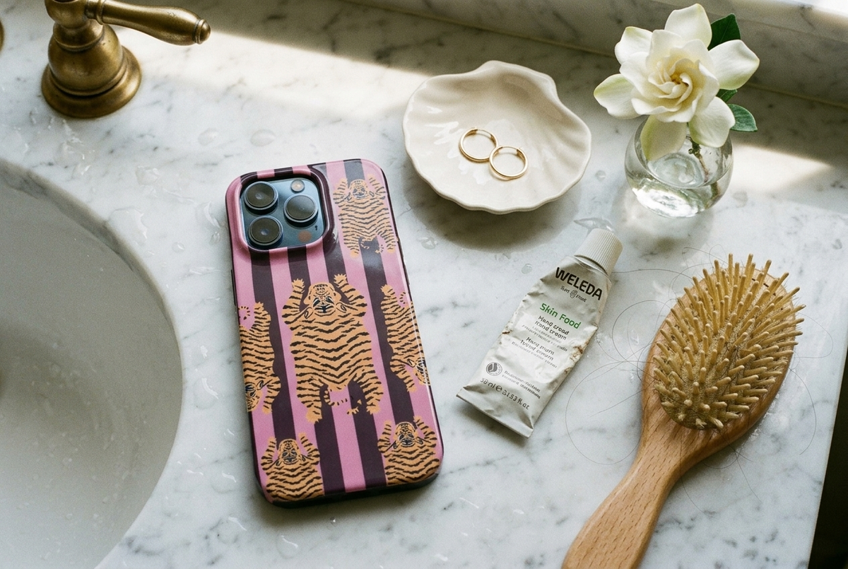 The Tibetan Tiger iPhone Case in Mauve Plum on a white marble bathroom counter with gold hoops and gardenia