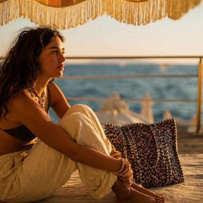 The Velvet Leopard Tote in pink leopard velvet, handmade and ethically made in Rajasthan, slumping softly on a deck at golden hour by the sea.